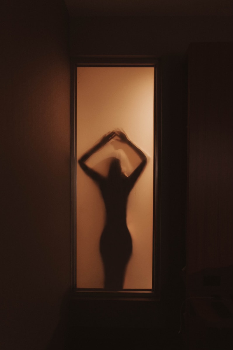 Photo by Jayson Hinrichsen a woman standing in front of a window in a dark room